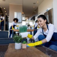 Professional Latin American cleaner cleaning a coffee table at a house and smiling - housework concepts